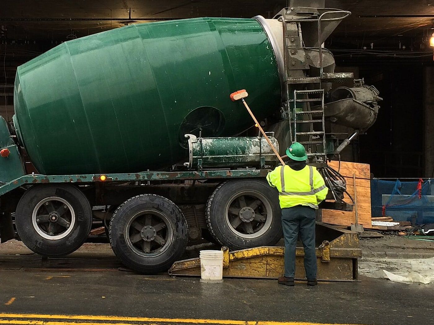 The drum of a green mixer truck being hosed down at a site entrance